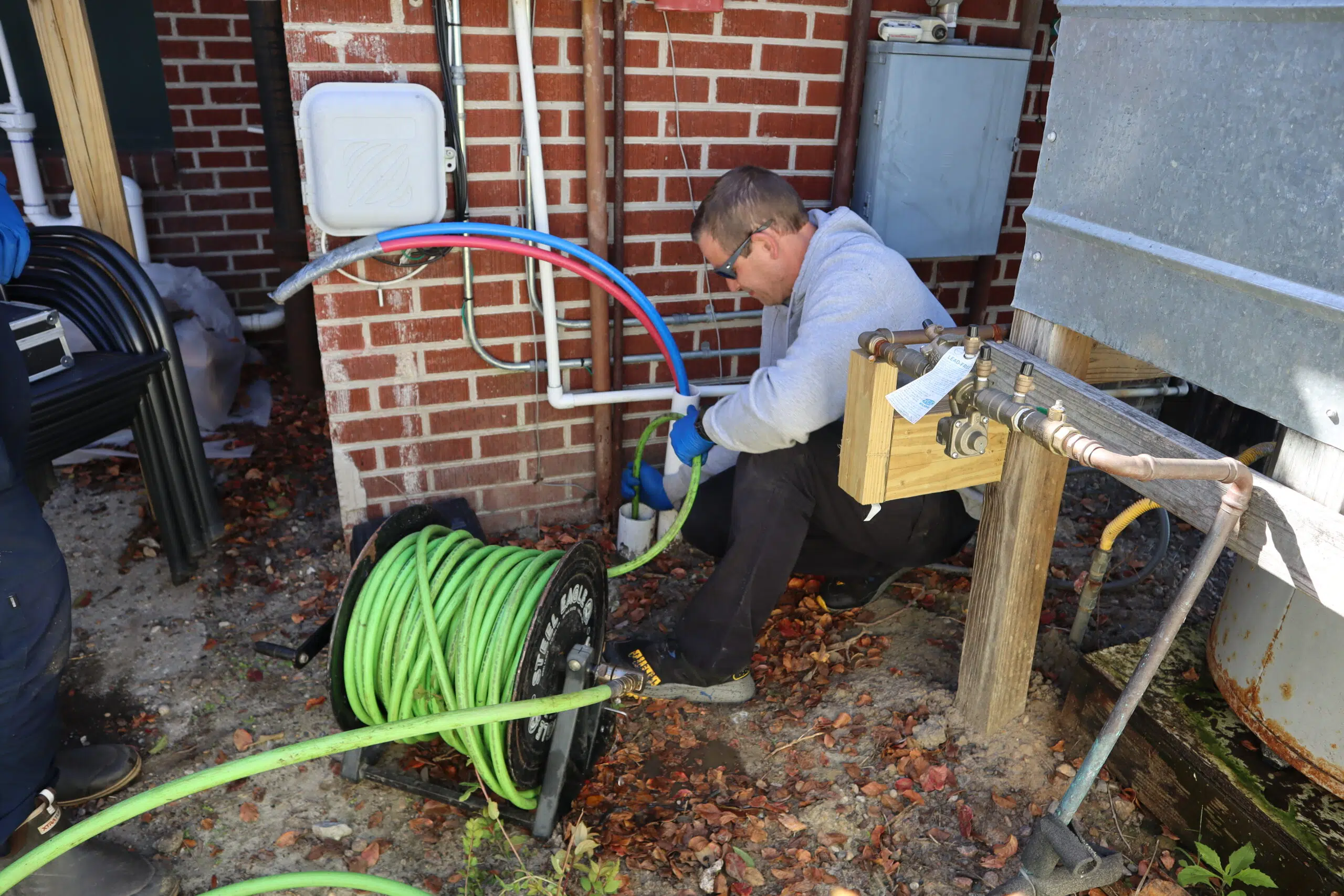 Rooter Man technician performing backflow testing and plumbing maintenance outside a brick home in Charleston, SC.