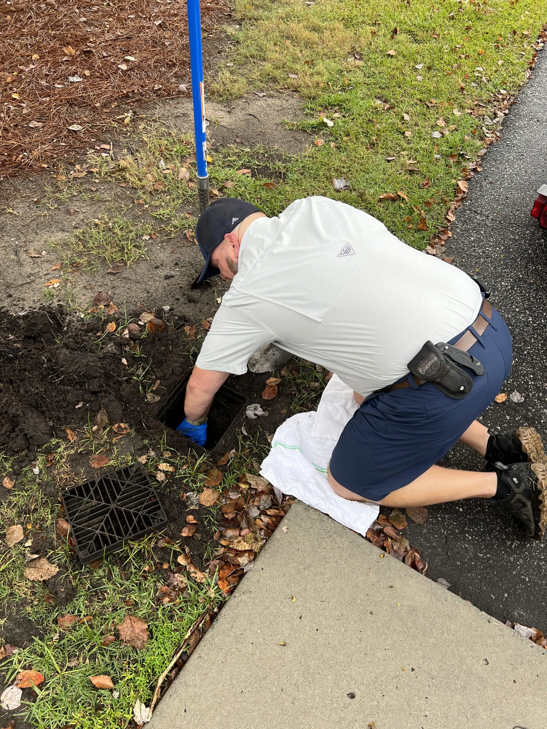 Rooter Man's plumbing tech Travis knelt over a hidden yard drain working on unclogging dirt and debris .
