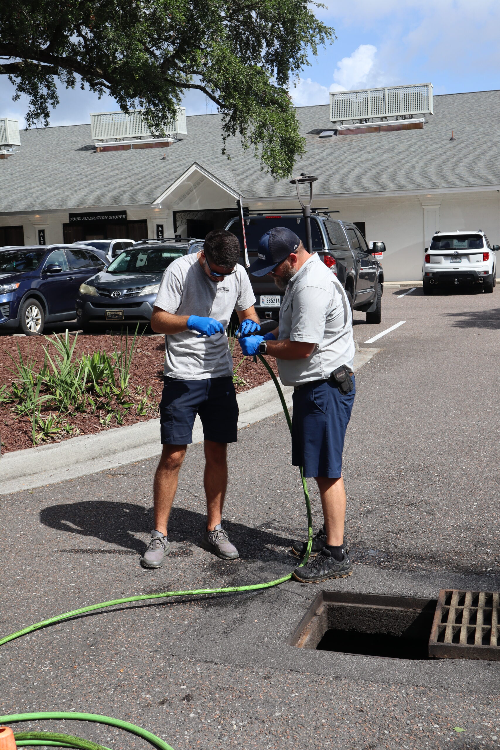 Rooter Man technicians preparing a hydro jetting hose while servicing a storm drain in a commercial parking lot.