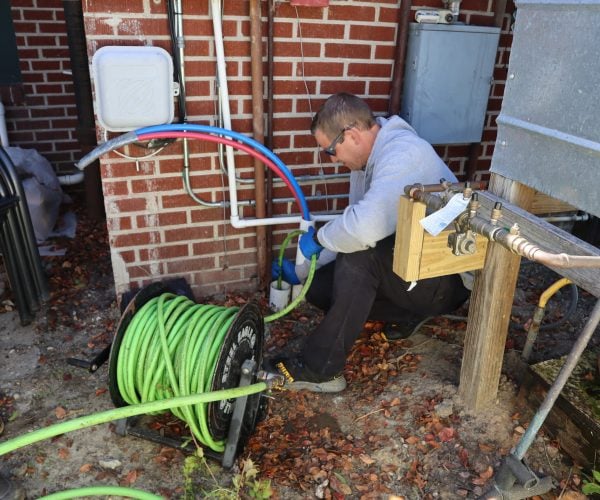 Rooter Man technician performing backflow testing and plumbing maintenance outside a brick home in Charleston, SC.