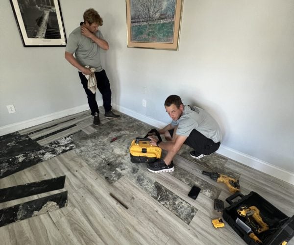 2 plumbing technicians working on repairing a slab leak located in the floor of an apartment living room.