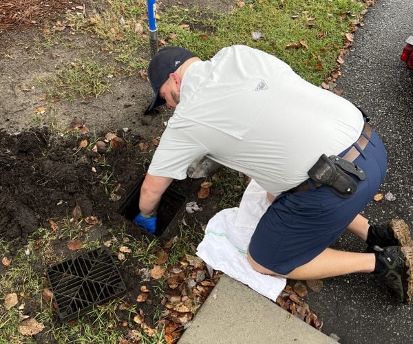 Rooter Man's plumbing tech Travis knelt over a hidden yard drain working on unclogging dirt and debris .